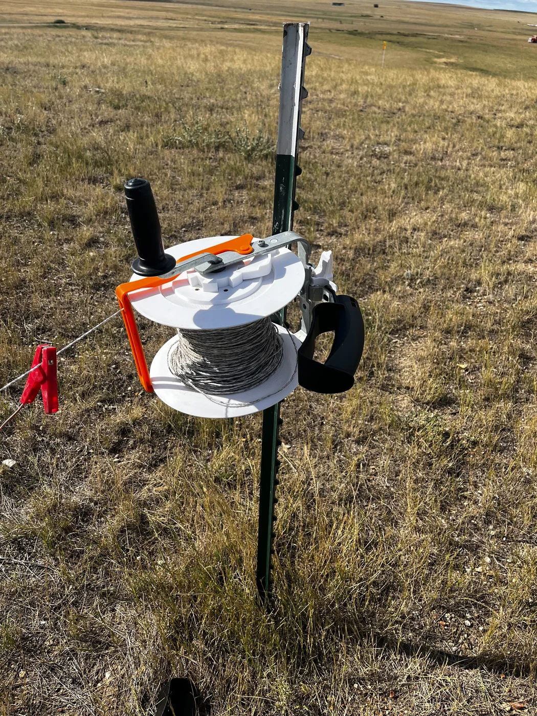 White 3D-printed electric fence reel operating on a pasture fence post
